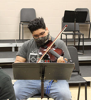 Male student practicing playing violin during class
